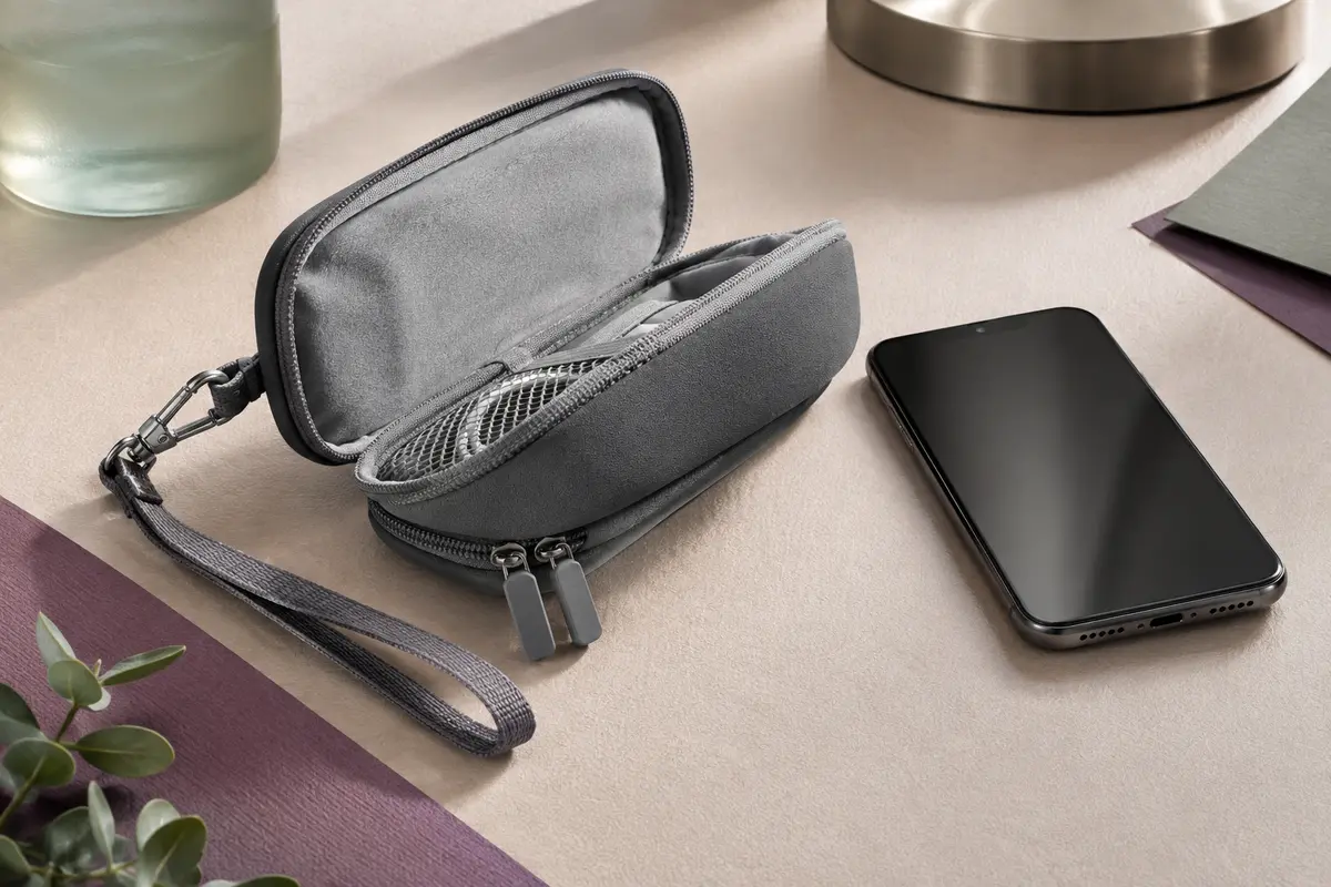 Pochette grise en néoprène ouverte près d’un smartphone sans marque, avec dragonne et mousqueton.